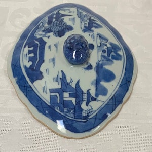 May include: A blue and white porcelain lid with a scalloped edge and a knob on top. The lid features a Chinese landscape design with buildings and trees.
