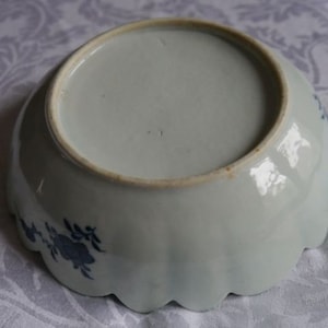 K&ouml;nnte beinhalten: Eine wei&szlig;e Keramikschale mit einem gewellten Rand und blauen Blumenmustern. Die Schale ist glasiert und hat eine glatte, gl&auml;nzende Oberfl&auml;che.