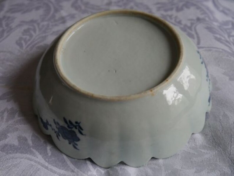 K&ouml;nnte beinhalten: Eine wei&szlig;e Keramikschale mit einem gewellten Rand und blauen Blumenmustern. Die Schale ist glasiert und hat eine glatte, gl&auml;nzende Oberfl&auml;che.
