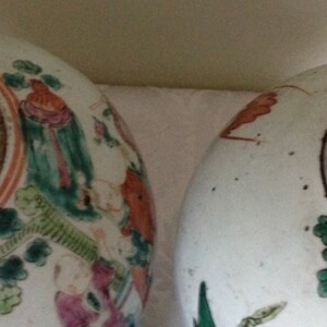 May include: Two white ceramic jars with lids, decorated with floral and figural designs in shades of green, red, and orange. The jars have a black interior.