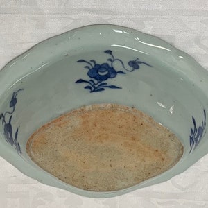 May include: A white ceramic bowl with a blue and white floral design. The bowl has a scalloped edge and a slightly raised rim. The bowl is in good condition with no chips or cracks.