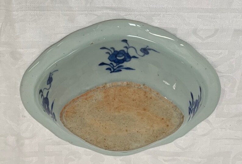 May include: A white ceramic bowl with a blue and white floral design. The bowl has a scalloped edge and a slightly raised rim. The bowl is in good condition with no chips or cracks.