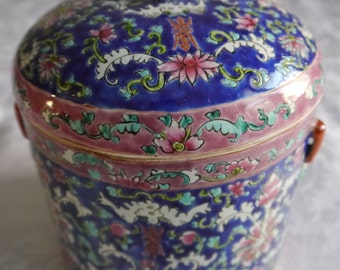 May include: A blue and white porcelain jar with a lid. The jar is decorated with floral patterns and has a green knob on the lid. The jar has two handles on the sides.