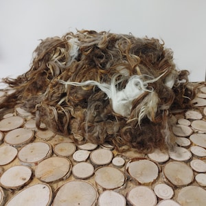 May include: A pile of brown and white wool fibers, likely from a sheep, on a background of wooden circles.
