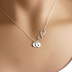May include: A silver necklace with an infinity symbol charm and two small round charms with the letters "K" and "E" engraved on them.