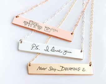 May include: Three horizontal bar necklaces in rose gold, silver, and gold tones. The rose gold bar features a child's drawing of a family and house. The silver bar is engraved with P.S. I love you. The gold bar reads Never Stop DREAMING.