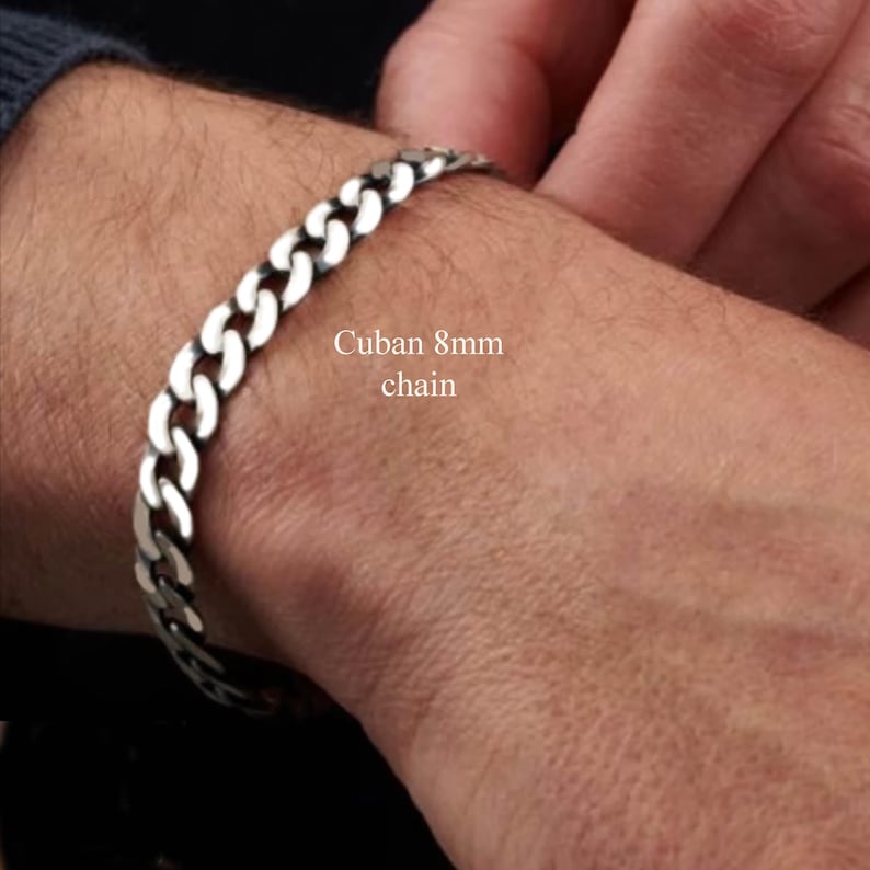 May include: A silver Cuban chain bracelet with a width of 8mm. The bracelet is on a person's wrist.