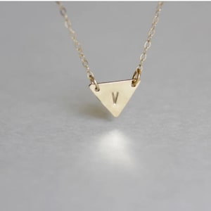 May include: A gold necklace with a small triangle pendant featuring the letter "V" engraved on it.