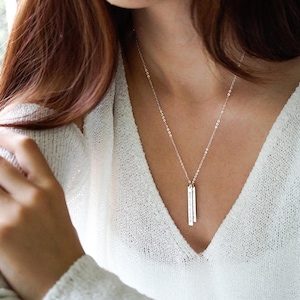 May include: A silver necklace with two vertical bar pendants. The necklace is worn by a person with long brown hair.