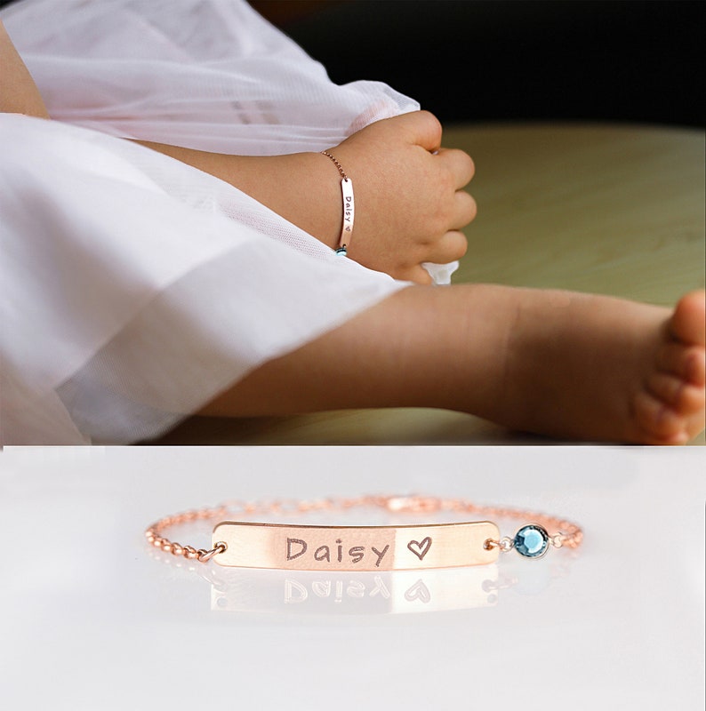 May include: A rose gold bracelet with a personalised nameplate that reads "Daisy" with a heart symbol. The bracelet has a small blue gemstone charm.