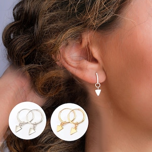 May include: Two pairs of gold hoop earrings with a small triangle charm hanging from each hoop. One pair of earrings is silver.