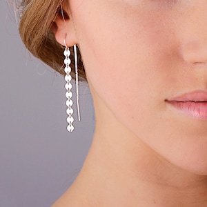 May include: Silver dangle earrings with a chain of small, round discs. The earrings are long and delicate.