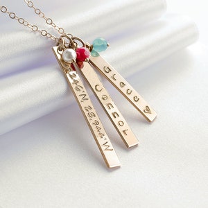 May include: Gold necklace with three bar pendants. The pendants are engraved with the words "Joescol", "Bless", and "32.46&deg;N 28.9444&deg;W". The necklace also features a small pearl and a red and blue gemstone.