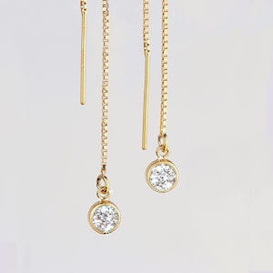 May include: A pair of gold chain earrings with a small, clear gemstone at the end of each chain.