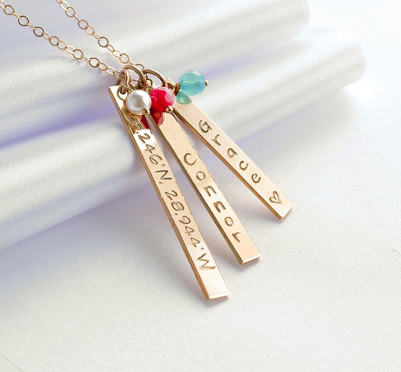 Op de afbeelding: Gouden ketting met drie staafvormige hangers. De hangers zijn gegraveerd met de woorden "Grace", "Jocelyn" en de co&ouml;rdinaten "24.46.N. 28.94.44.W".