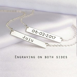 May include: Two silver-toned bar necklaces featuring delicate chains. One bar is engraved with the name Juju, and the other bar displays the date 08.02.2017. The text Engraving on both sides is visible below the jewelry pieces.