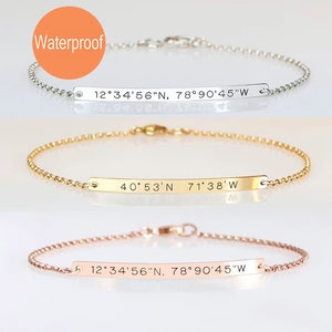 May include: Three delicate chain bracelets with horizontal metal bars. The top bar is silver-toned, the middle is gold-toned, and the bottom is rose gold-toned. Each bar is engraved with coordinates. An orange circle with the text Waterproof.