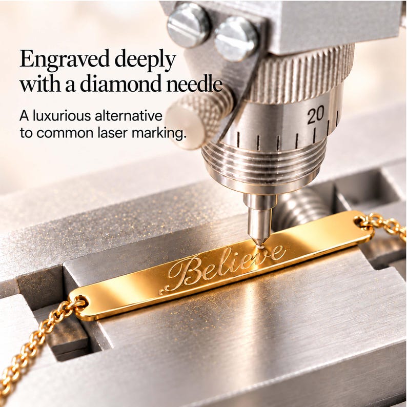 May include: A gold-toned metal bar bracelet with the word Believe engraved on its surface. A diamond-tipped needle is positioned above the bracelet, which is held in a metal clamp. Text reads: Engraved deeply with a diamond needle. A luxurious alternative to common laser marking.