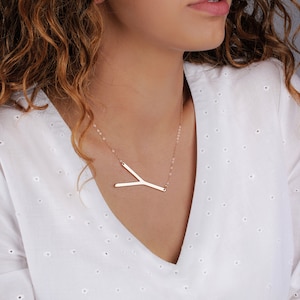 May include: A gold necklace with a Y-shaped pendant. The necklace is on a model wearing a white shirt.