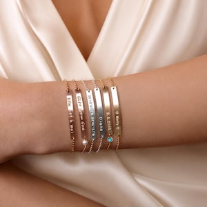 May include: A set of six thin metal bar bracelets with delicate ball chains. Each bar features custom engravings including text like Elle est &agrave; moi, Gift from God, coordinates, Diana, 9.5.2015, and Molly with hearts, plus small pearl and blue stone accents.