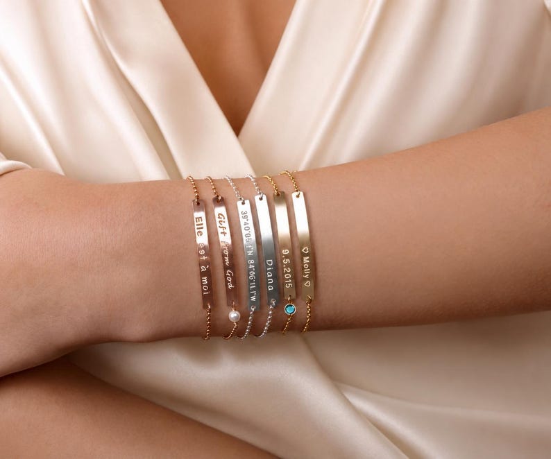 May include: A set of six thin metal bar bracelets with delicate ball chains. Each bar features custom engravings including text like Elle est &agrave; moi, Gift from God, coordinates, Diana, 9.5.2015, and Molly with hearts, plus small pearl and blue stone accents.