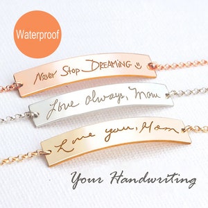May include: Three gold, silver, and rose gold bracelets with curved bars engraved with handwritten messages. The bracelets are on a white background. The text on the bracelets reads "Never Stop Dreaming", "Love always, Mom", and "Love you, Mom".