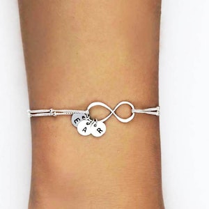 May include: A silver infinity bracelet with three charms, each with a letter on it. The letters are E, A, and R.