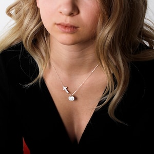 May include: A silver necklace with a small cross charm and a round charm with the letter 'D' engraved on it.
