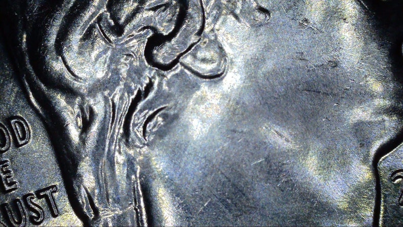 May include: Close-up of a silver coin with the words "In God We Trust" and a portrait of a person's profile.