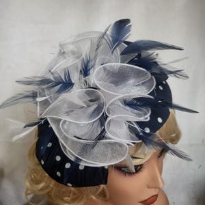 Peut inclure: Un fascinateur bleu marine à pois blancs avec des plumes blanches et bleu marine et un design en tissu blanc transparent à volants. Ce couvre-chef est adapté aux occasions spéciales.