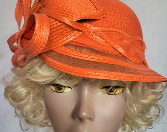 Elevate your look with our captivating pillbox-style orange hat featuring stunning feather accents.