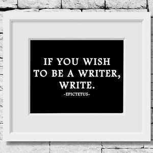 May include: A white rectangular frame containing a black print with the white text: IF YOU WISH TO BE A WRITER, WRITE. -EPICTETUS-. The frame features a wide white mat border surrounding the central black rectangular area with the quote.