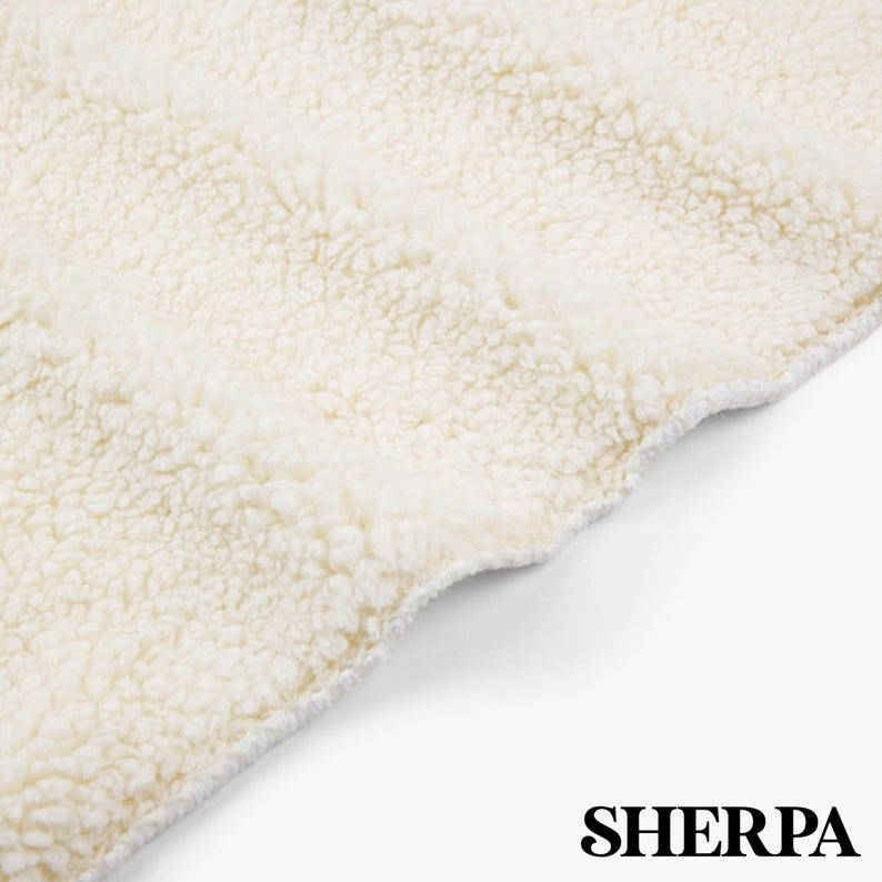 May include: Close-up of a cream-colored Sherpa fabric. The material has a soft, textured appearance with a wavy edge. The word "SHERPA" is printed in a bold, black font at the bottom of the image. This fabric is ideal for blankets and throws.