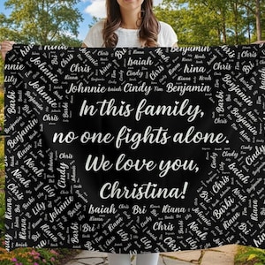 May include: A black blanket with white text. The blanket reads "In this family, no one fights alone. We love you, Christina!" with names scattered around the border. A woman holds the blanket in a garden.