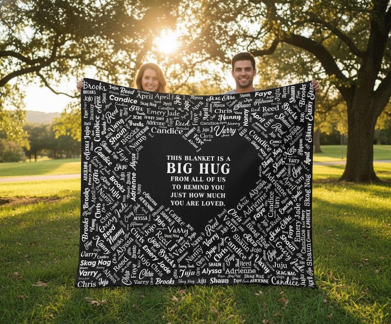 May include: A black blanket with a heart-shaped design in the center, surrounded by names in white. The text in the heart reads, "THIS BLANKET IS A BIG HUG FROM ALL OF US TO REMIND YOU JUST HOW MUCH YOU ARE LOVED."
