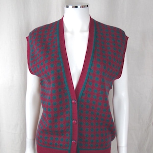 May include: A sleeveless, button-down sweater vest in a burgundy and teal geometric pattern. The vest has a V-neck and is displayed on a mannequin. The vest is paired with blue jeans.