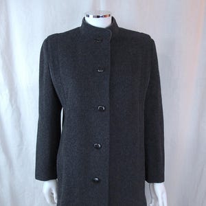 May include: A dark gray wool coat with a mandarin collar and button-down front. The coat has long sleeves and a tailored fit, displayed on a mannequin. The coat is paired with blue jeans.