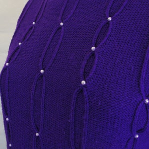 Puede incluir: Un su&eacute;ter de punto morado con un patr&oacute;n de punto de cable y adornos de perlas.