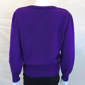 Puede incluir: Un su&eacute;ter de punto morado con mangas largas y cuello redondo. El su&eacute;ter tiene un dobladillo y pu&ntilde;os de canal&eacute;.