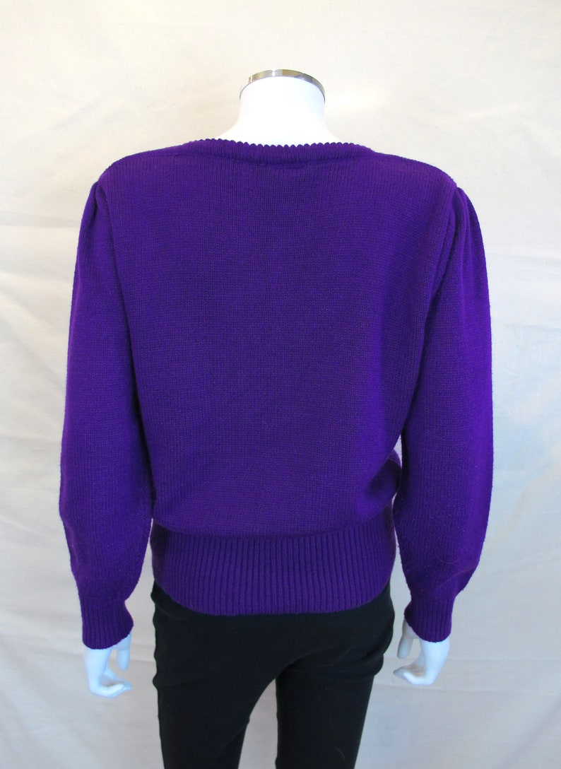 Puede incluir: Un su&eacute;ter de punto morado con mangas largas y cuello redondo. El su&eacute;ter tiene un dobladillo y pu&ntilde;os de canal&eacute;.