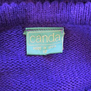 Puede incluir: Un su&eacute;ter de punto morado con una etiqueta verde que dice "canda" y "made in korea" en texto blanco.