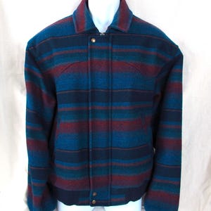 May include: A blue, teal, and burgundy striped jacket with a collared neckline and button closure. The jacket has a ribbed hem and cuffs. The jacket is made of a thick, woven material.