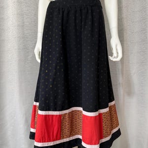 May include: A black midi skirt featuring a small gold star pattern throughout. The hem is accented with a horizontal band of light pink fabric, followed by alternating panels of solid red fabric and a brown fabric with a geometric pattern.