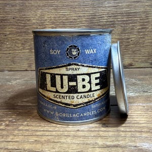May include: A blue soy wax scented candle in a metal tin with the text "LU-BE" in a black and white label. The lid is off to the side. The candle is from Gorilla Candles.