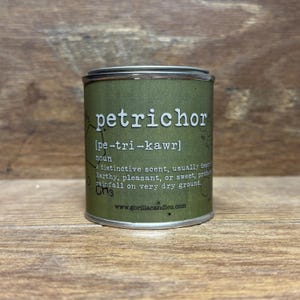 May include: A green cylindrical candle tin with the word "petrichor" in white, along with its pronunciation and definition. The text describes the scent as earthy, pleasant, or sweet, often associated with rainfall. The website www.gorillacandles.com is also visible.