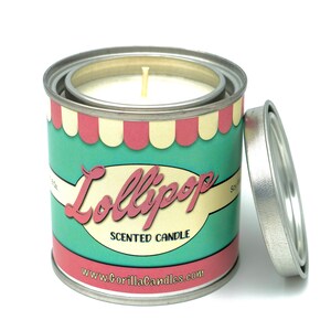 Peut inclure: Une bougie blanche dans une boîte en métal avec un couvercle rayé turquoise et rose. La boîte porte l'inscription "Lollipop Scented Candle" et "www.GorillaCandles.com".
