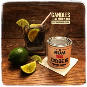 May include: A silver can with a brown label that reads "Gorilla Candles Rum and Coke" with a glass of cola and lime wedges on a wooden surface. The text "Candles That Men Want" and "www.gorillacandles.com" is displayed above the image.