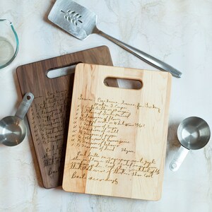 Pode incluir: Duas t&aacute;buas de corte de madeira com receitas manuscritas, um copo medidor transparente, uma esp&aacute;tula de metal e uma x&iacute;cara de medi&ccedil;&atilde;o de metal. Uma t&aacute;bua &eacute; clara, a outra &eacute; escura. A esp&aacute;tula tem um desenho de folha.