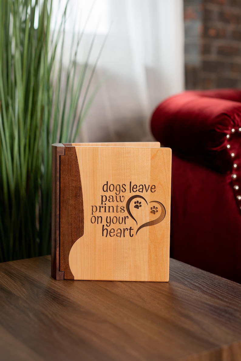 May include: A wooden box with a light wood front and a dark wood side. The front of the box has the words "dogs leave paw prints on your heart" with paw prints inside a heart shape. The box is sitting on a wooden surface.