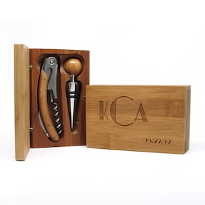 May include: A bamboo wine tool set with a corkscrew and bottle stopper. The set includes a wooden box with the initials "KCA" and the date "06.22.02" engraved on the front. The corkscrew and stopper are made of metal and wood.